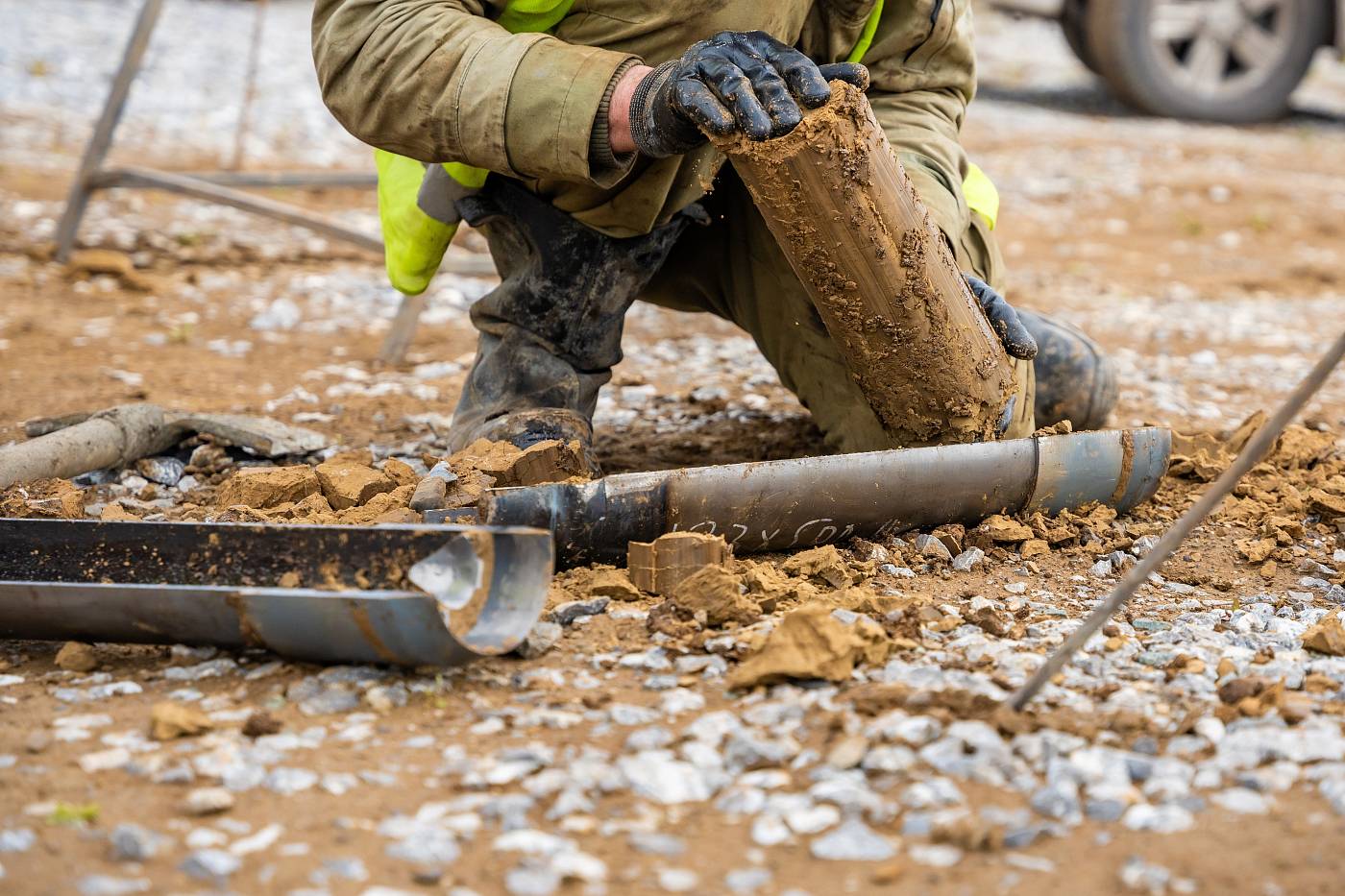 Eine Person entnimmt auf einer Baustelle mit Schutzhandschuhen eine Bodenprobe aus einem Bohrkern.