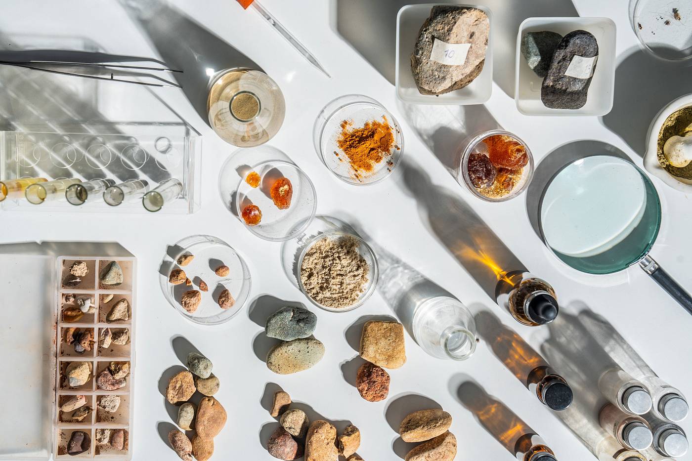 Laborarbeitsplatz mit verschiedenen Gesteins- und Bodenproben, Petrischalen, Reagenzgläsern und Lupen für geowissenschaftliche Untersuchungen.