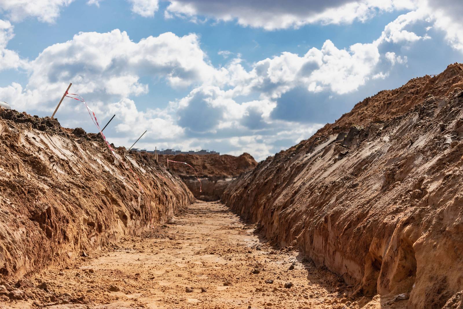 Offene Baugrube mit freigelegten Erdschichten unter blauem Himmel
