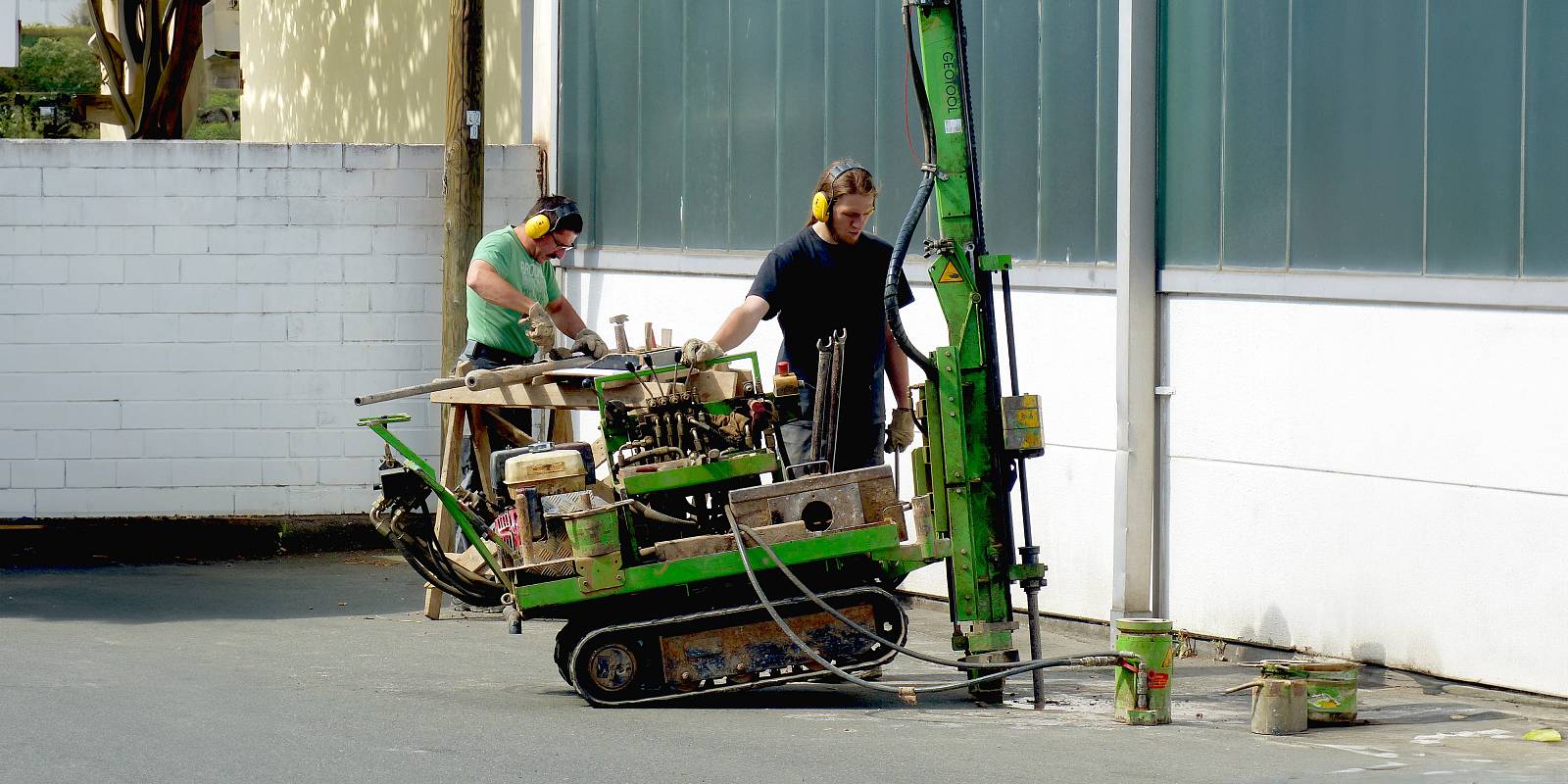 Zwei Arbeiter führen mit einem kompakten Bohrgerät Bohrungen im Außenbereich durch.