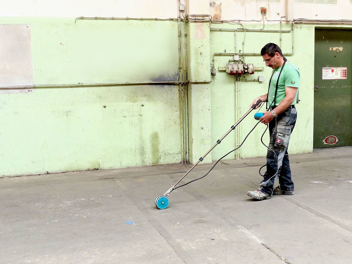Mann in Arbeitskleidung führt in einer Industriehalle eine Bodenuntersuchung mit einem Georadar durch.
