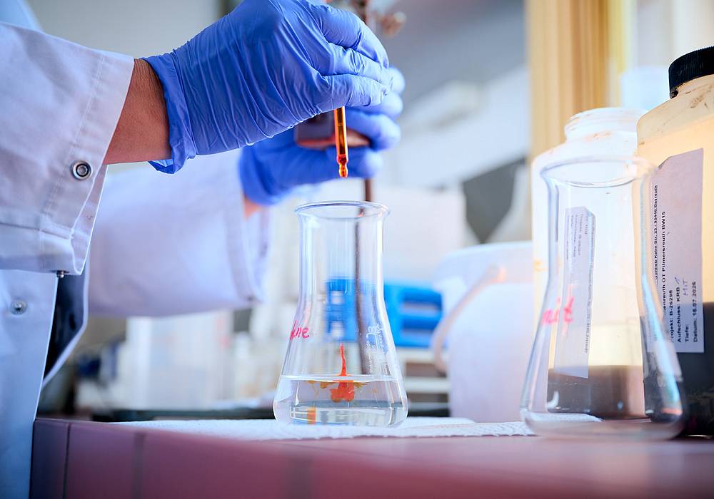 Laborarbeit bei gabex engineers: Eine Probe wird mit einer Pipette in einen Glaskolben gegeben.