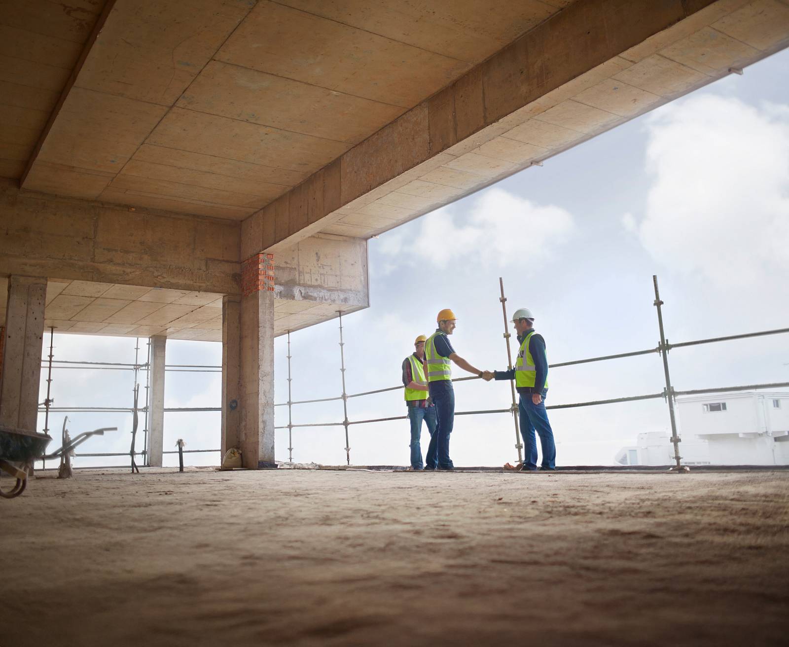 Bauingenieure mit Schutzhelmen und Warnwesten geben sich im Rohbau die Hand.