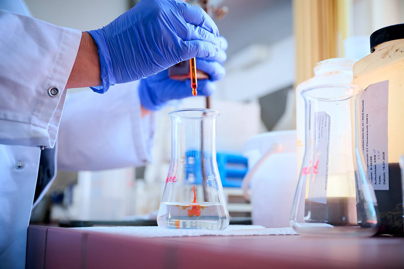 Laboruntersuchung einer Wasserprobe bei gabex engineers mit Pipette, Schutzkleidung und Glasgefäßen.
