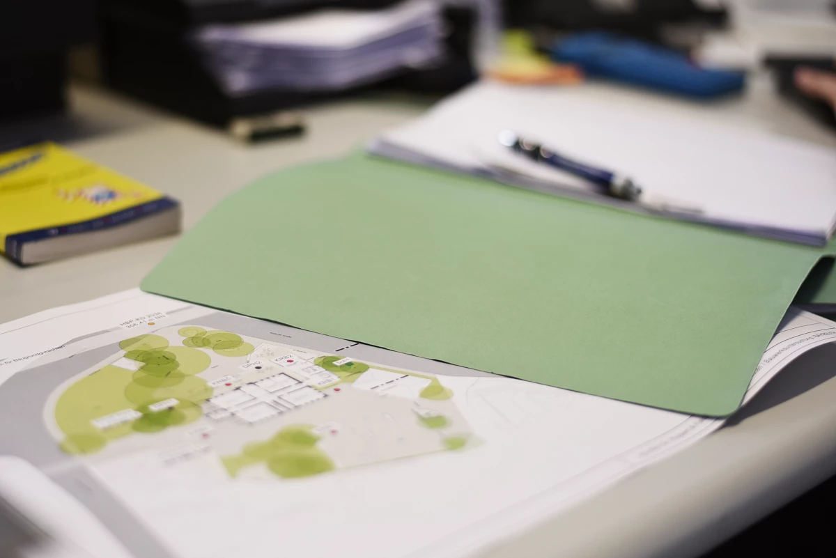 Geöffnete grüne Aktenmappe mit Bauplänen und Notizen auf einem Schreibtisch im Ingenieurbüro.