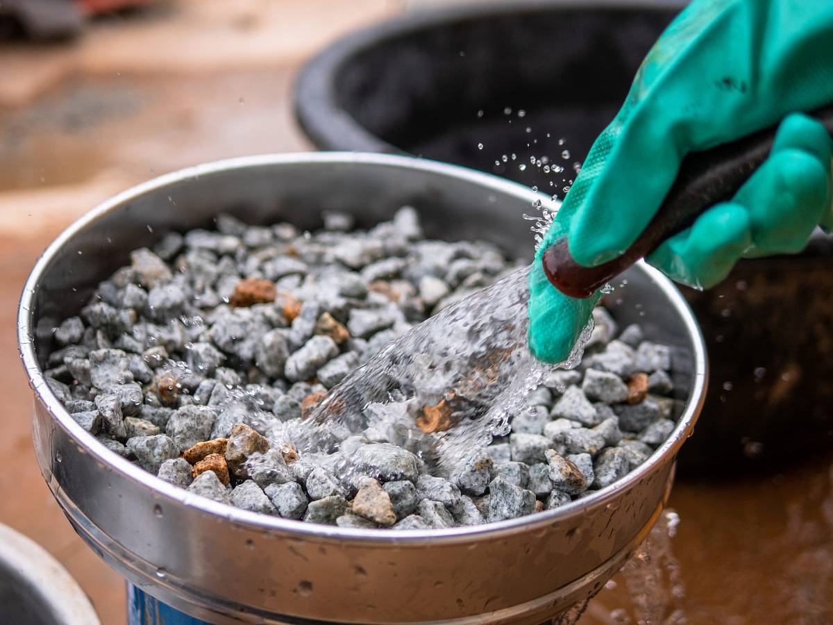 Laborarbeiter reinigt Gesteinsproben mit Wasserstrahl für die anschließende Analyse.