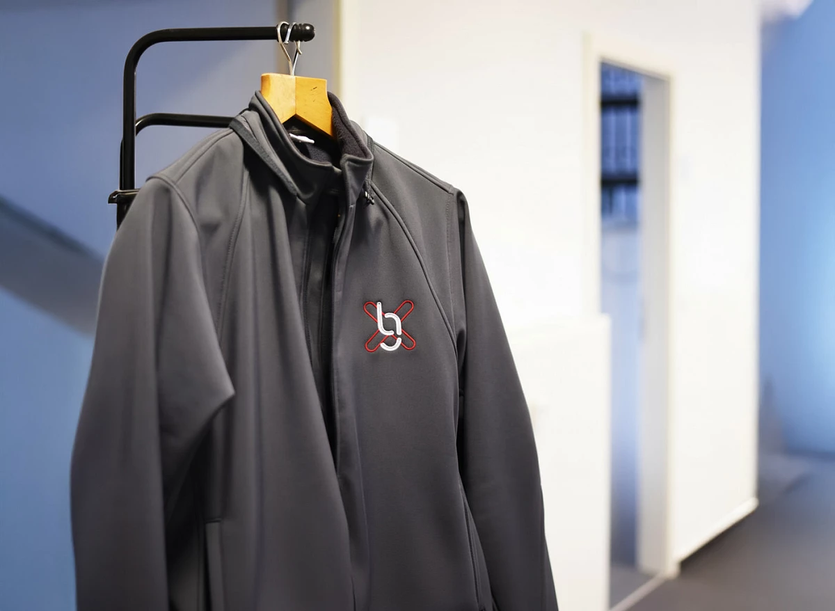 Dunkelgraue Softshelljacke mit dem Logo von gabex engineers hängt auf einem Kleiderständer im Büro.