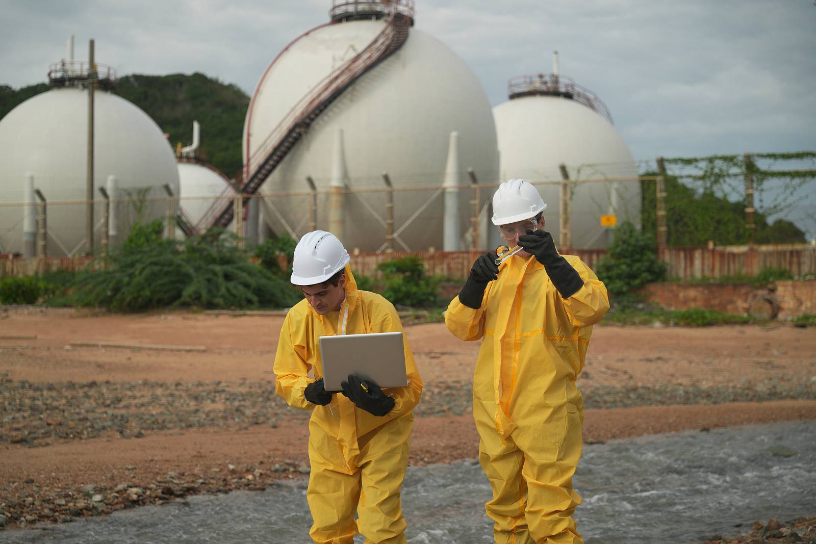 Experten in Schutzanzügen untersuchen Wasserqualität bei Industrieanlage.