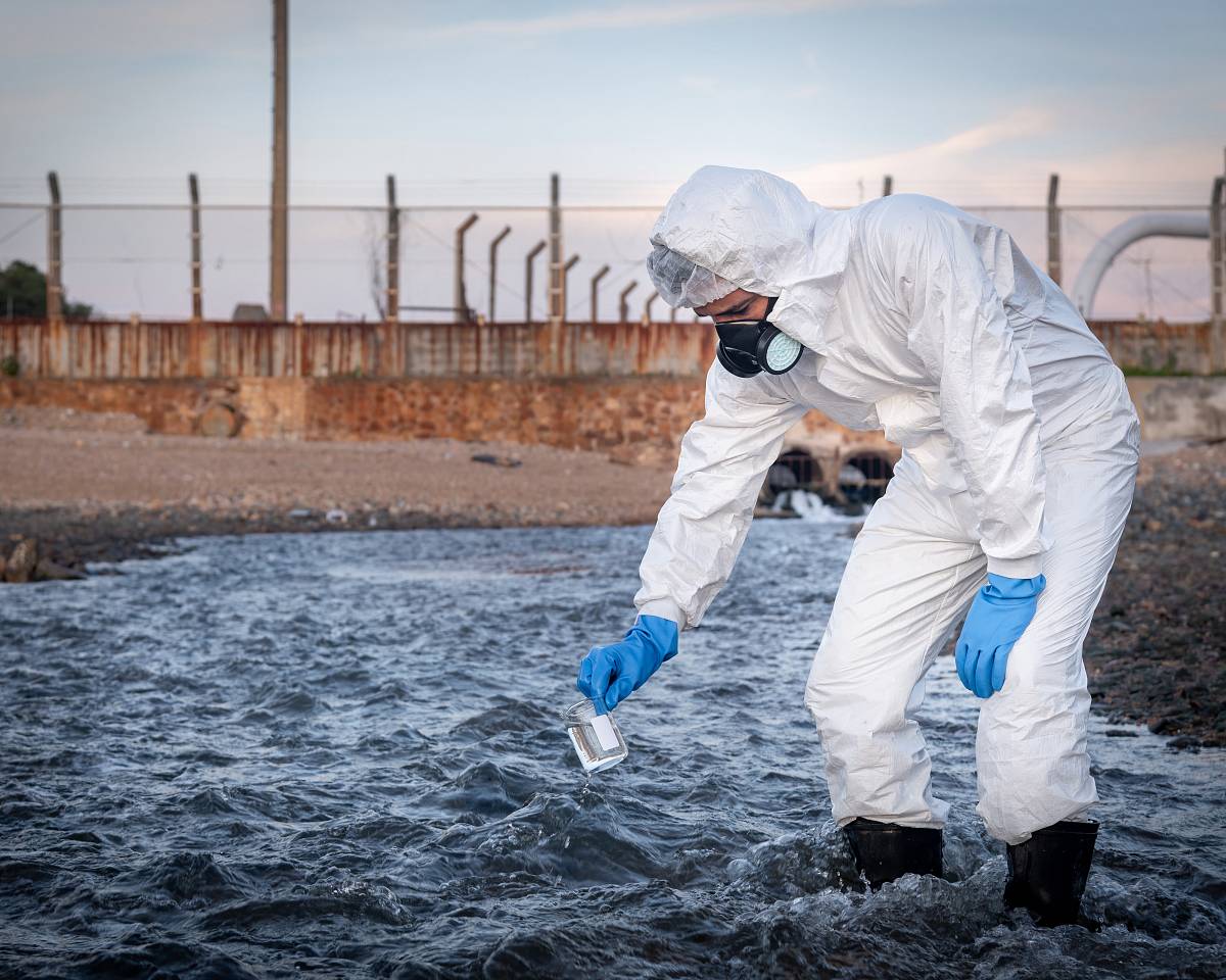 Person in Schutzanzug entnimmt Wasserprobe zur Kontrolle der Grundwasserqualität.