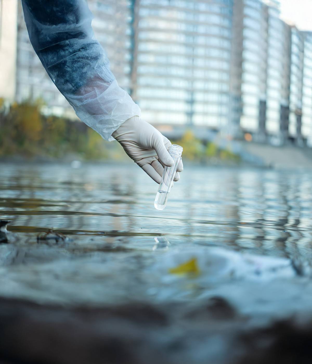 Hand mit Schutzhandschuh entnimmt Wasserprobe zur Analyse der Wasserqualität.