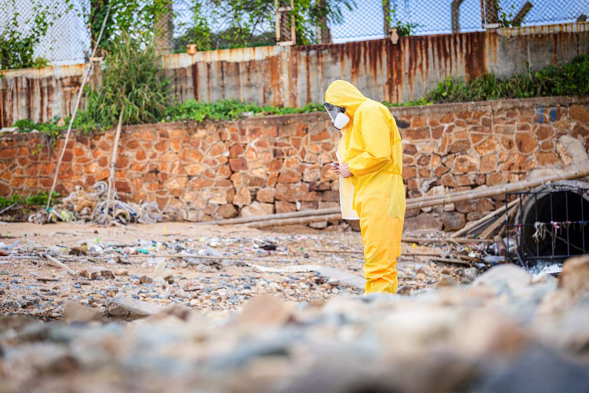 Person in Schutzanzug untersucht Boden und Wasser an einer möglichen Schadstoffquelle.