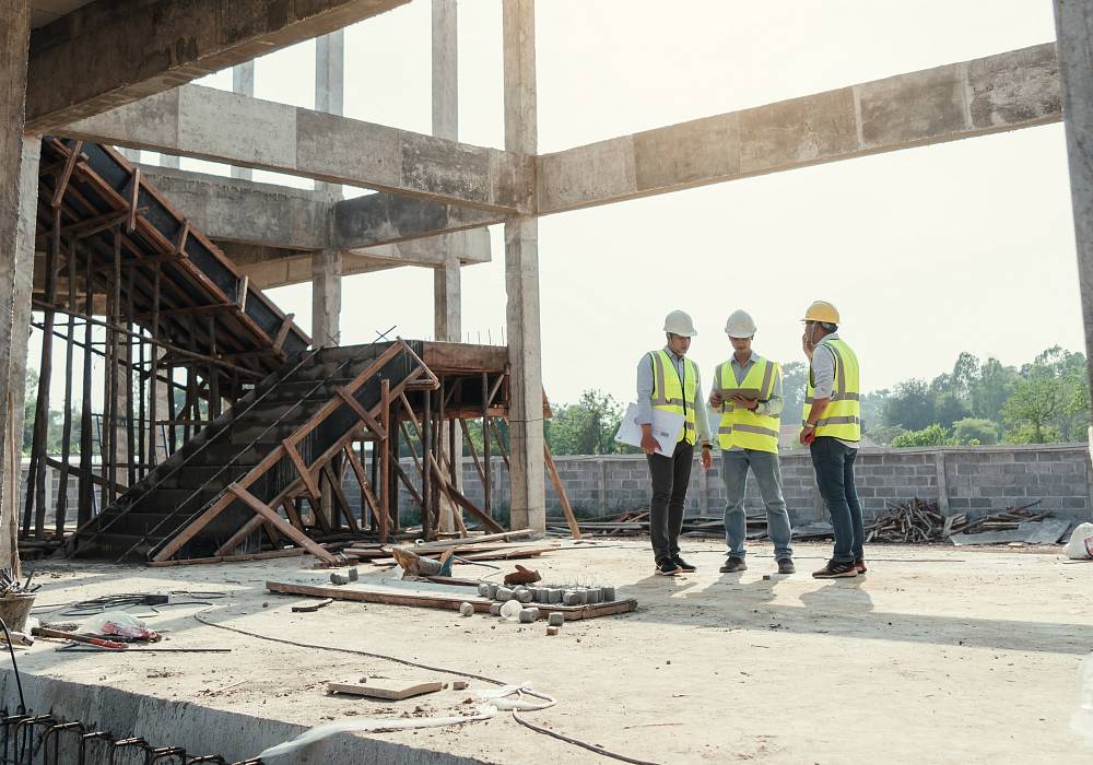 Drei Fachleute in Warnwesten und Schutzhelmen begutachten die Bausubstanz und Struktur eines Rohbaus im Rahmen einer Bauwerksuntersuchung.