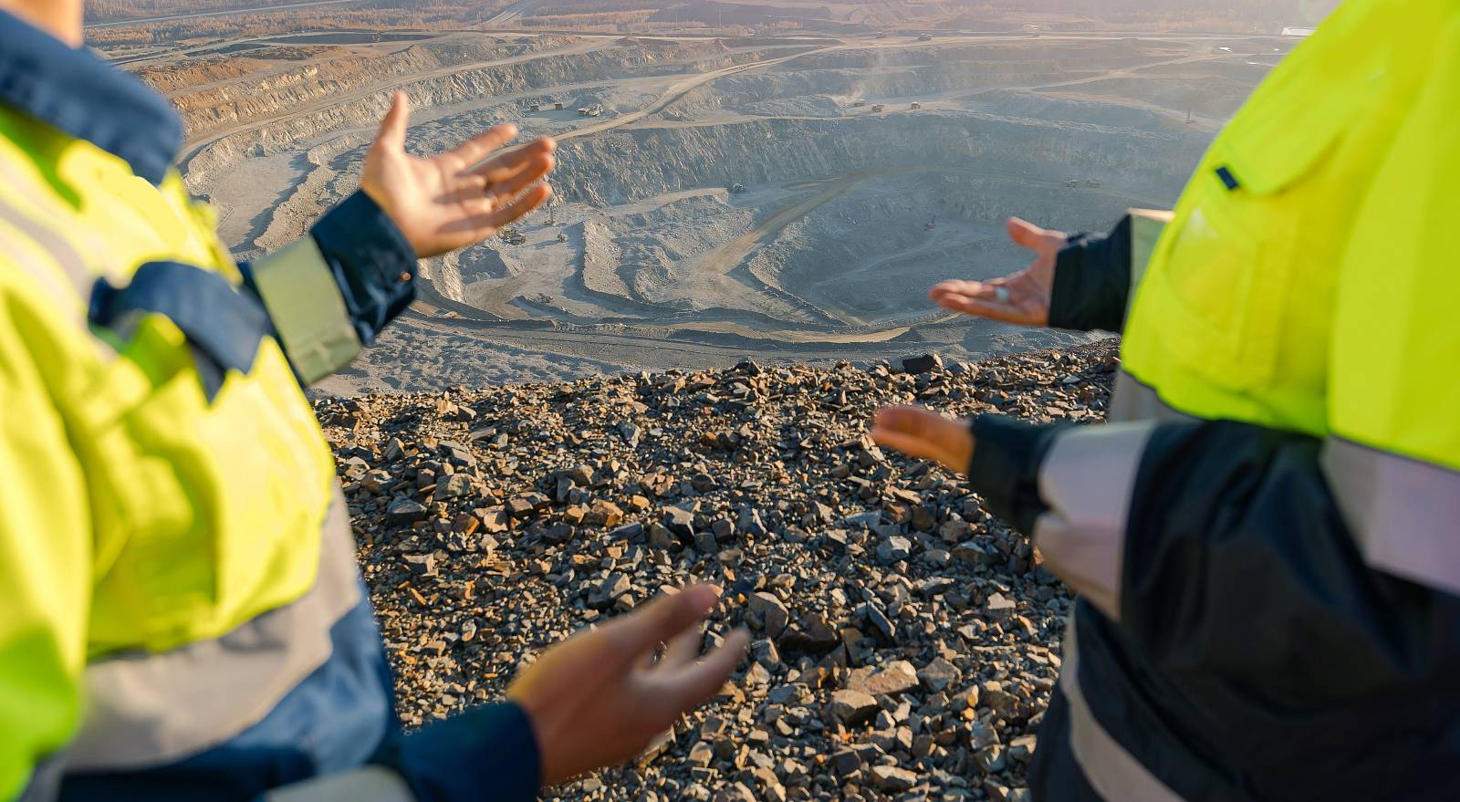 Zwei Ingenieure in Warnkleidung begutachten ein großes Erd- oder Tagebaugelände und besprechen die Boden- und Aushubbedingungen vor Ort.