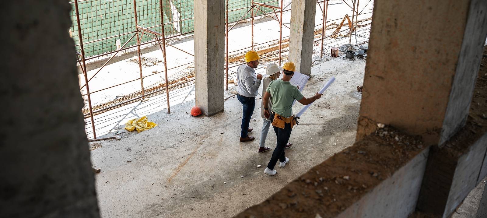 Drei Bauingenieure mit Schutzhelmen besprechen Pläne auf einer Baustelle.