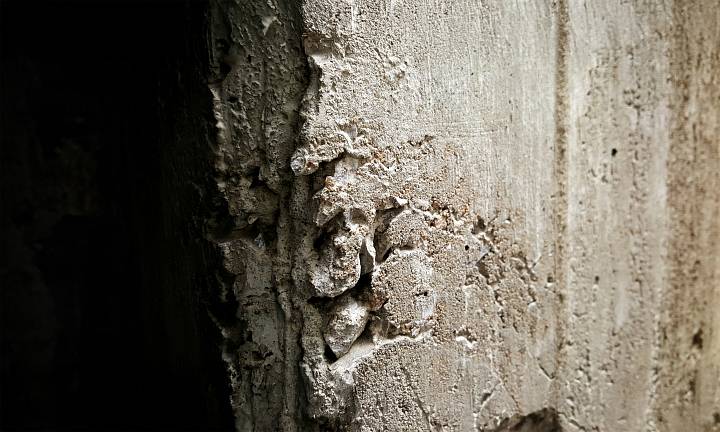 Nahaufnahme einer beschädigten Betonwand mit sichtbaren Rissen und Abplatzungen