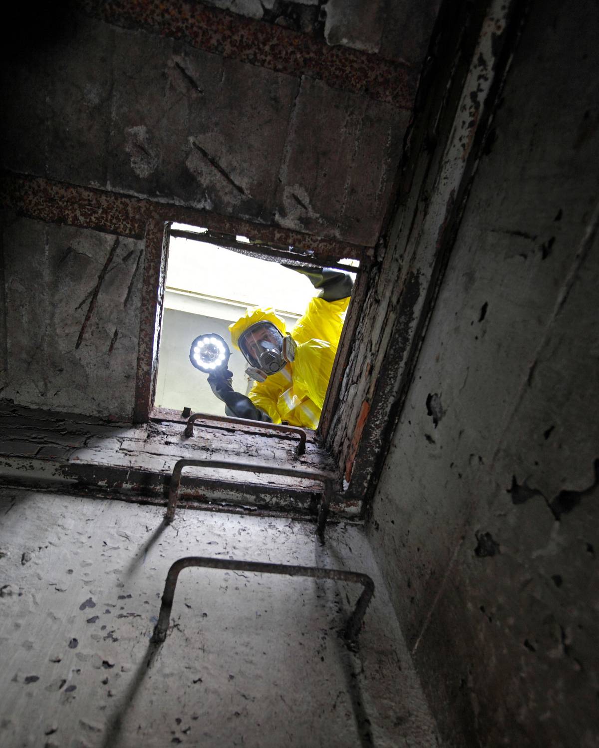 Fachkraft in Schutzanzug und Atemmaske untersucht einen kontaminierten Schacht mit Taschenlampe