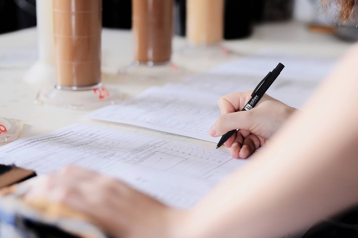 Person trägt Messwerte in ein Prüfprotokoll ein, im Hintergrund stehen Zylinder mit Sedimentproben.