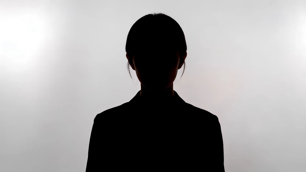 Dunkle Silhouette einer Person mit zurückgebundenem Haar vor hellem, neutralem Hintergrund.